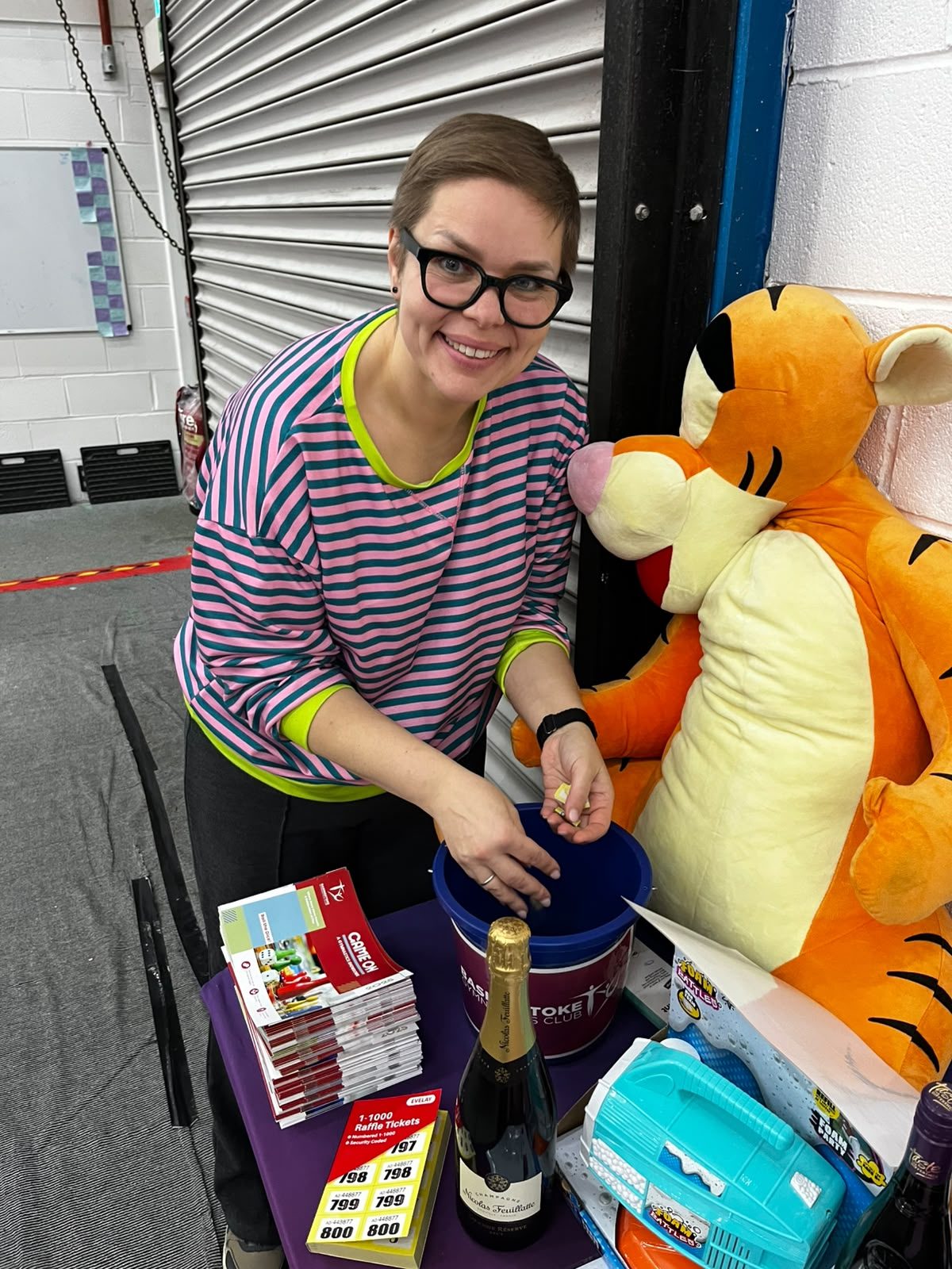 A Community Hub volunteer behind a tombola table stacked with donated prizes